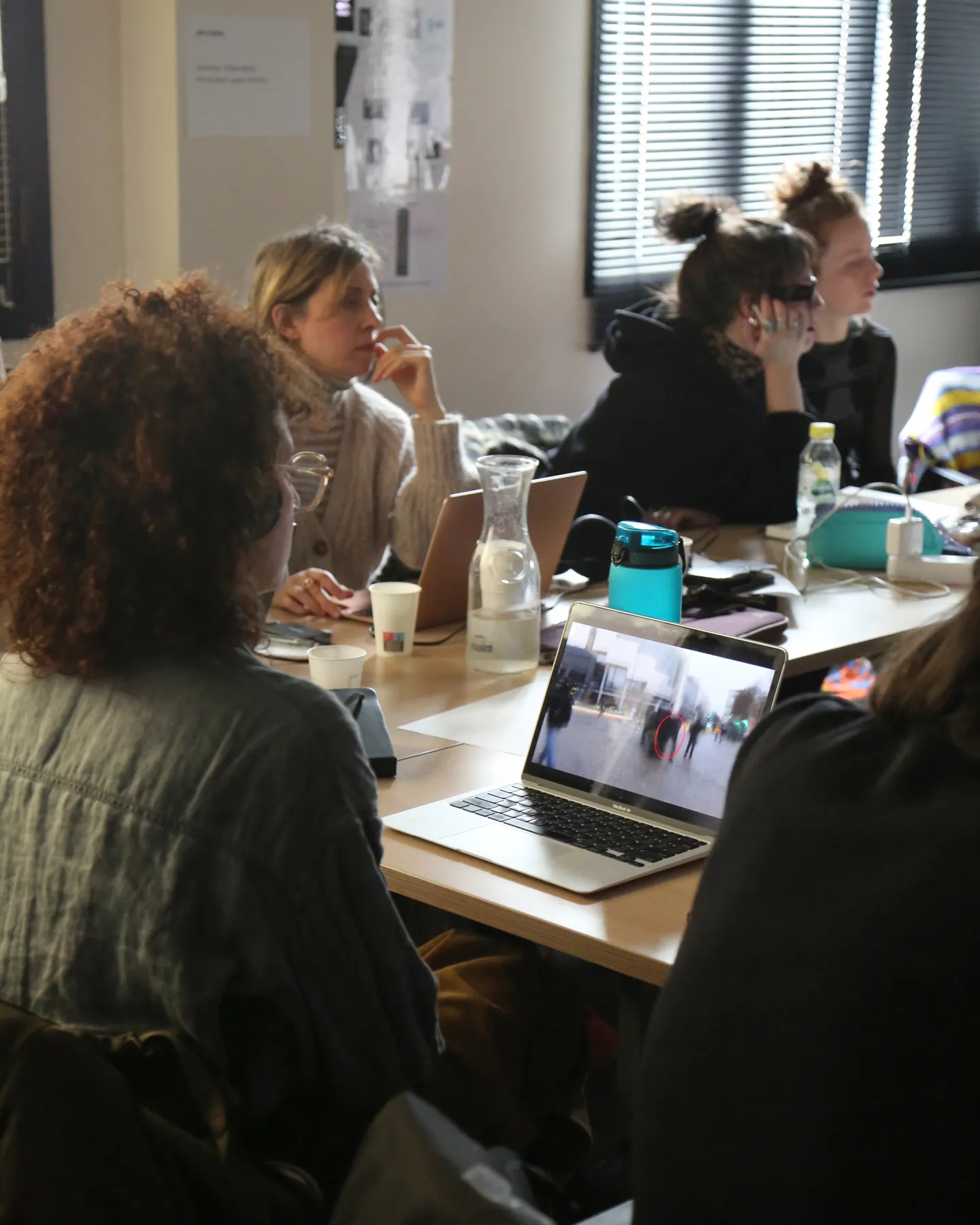 Participants gathered around a work table, a laptop displaying a video annotated with a red circle