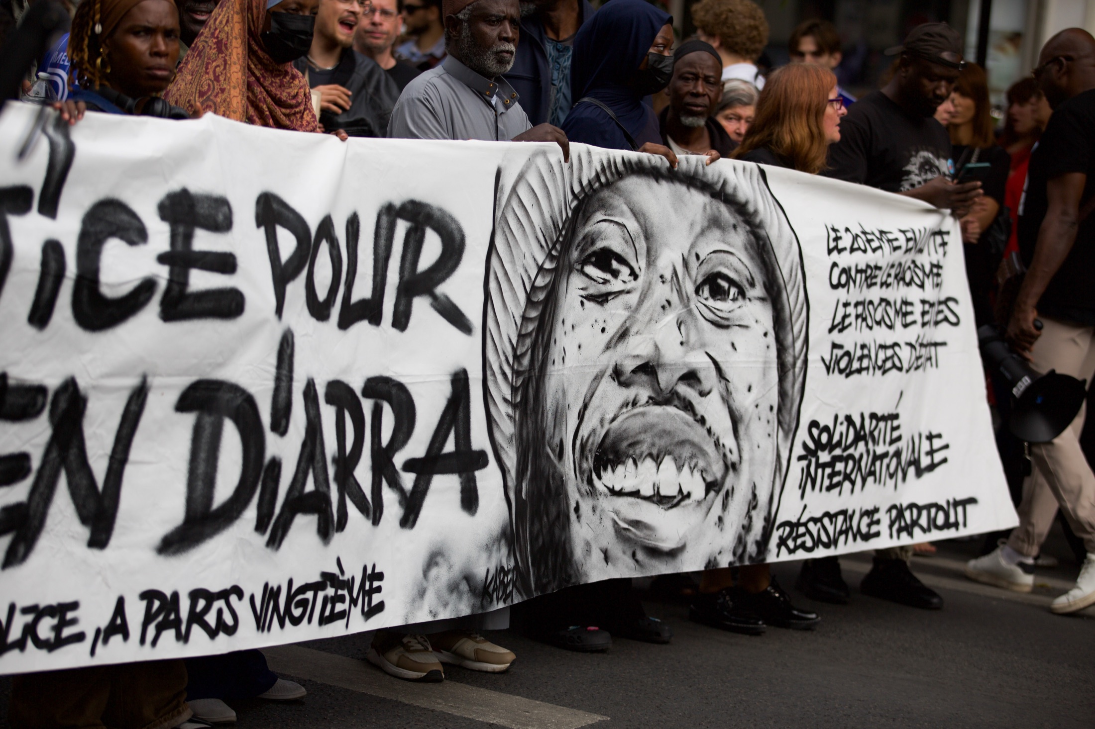 Des manifestant·es portent une banderole peinte « Justice pour Ben D’Arra », ornée d’un portrait au pochoir