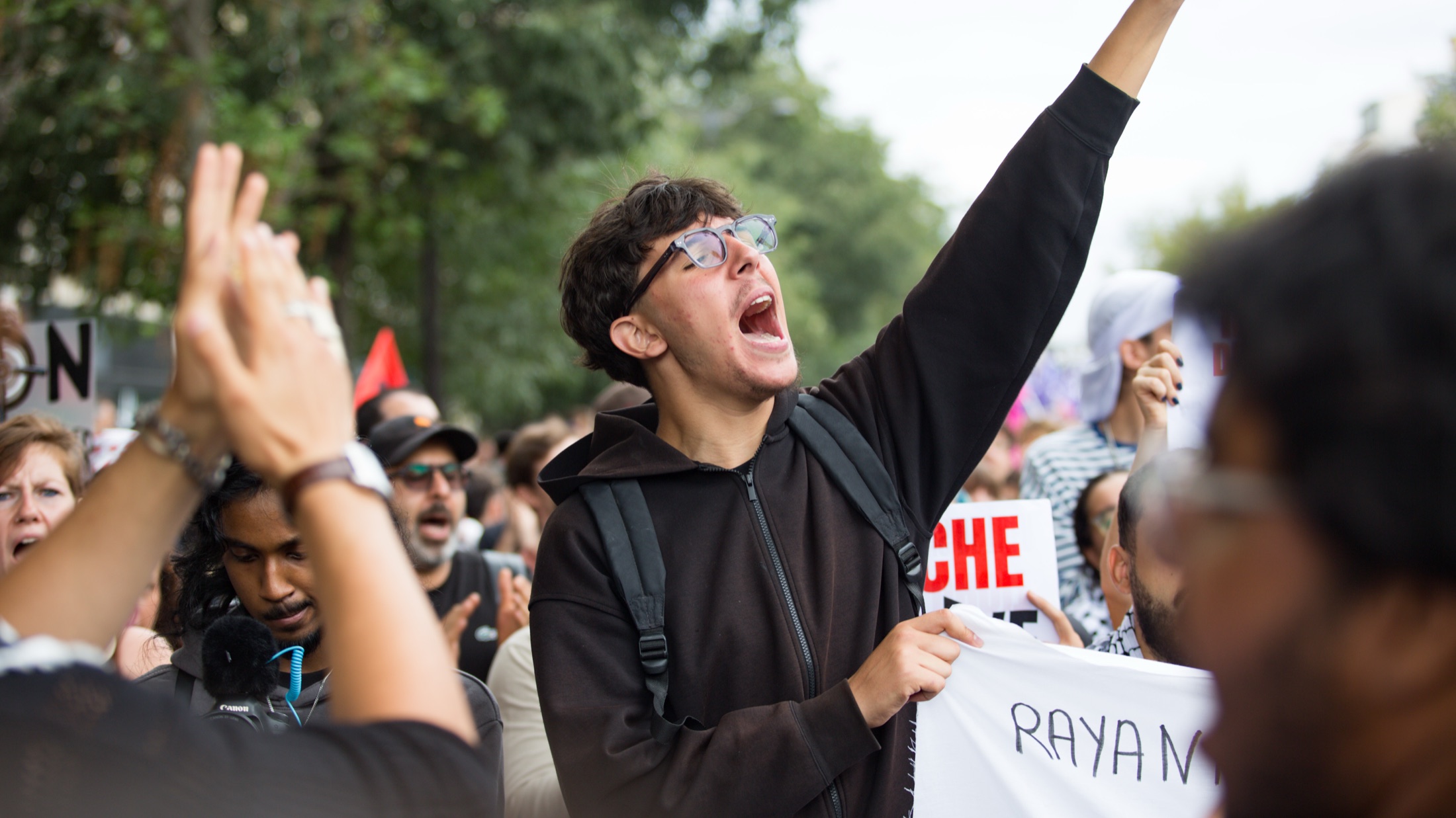 Un jeune manifestant crie un slogan, le bras levé, au milieu de la foule