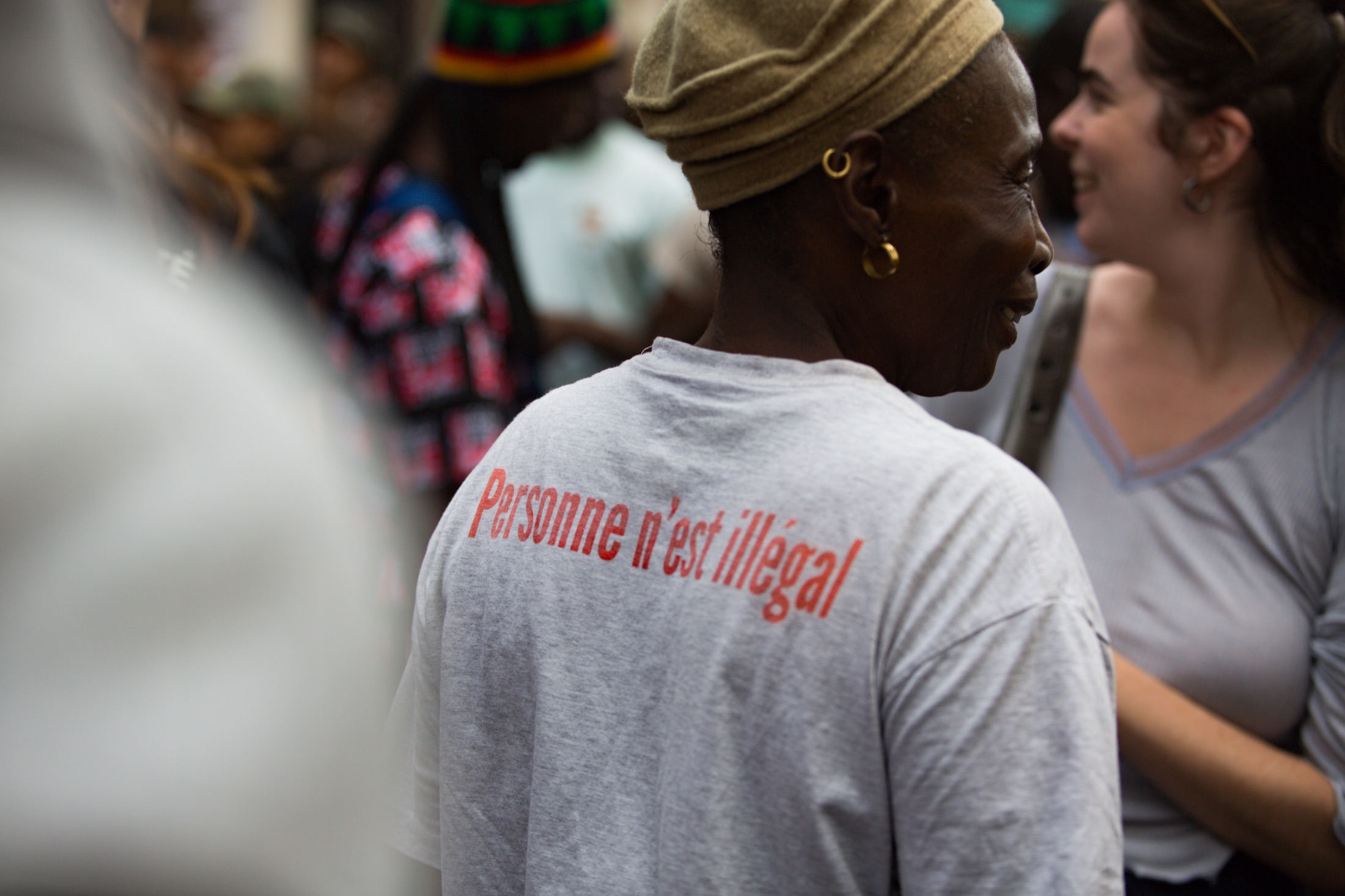 Une manifestante de dos porte un t-shirt floqué « Personne n’est illégal »