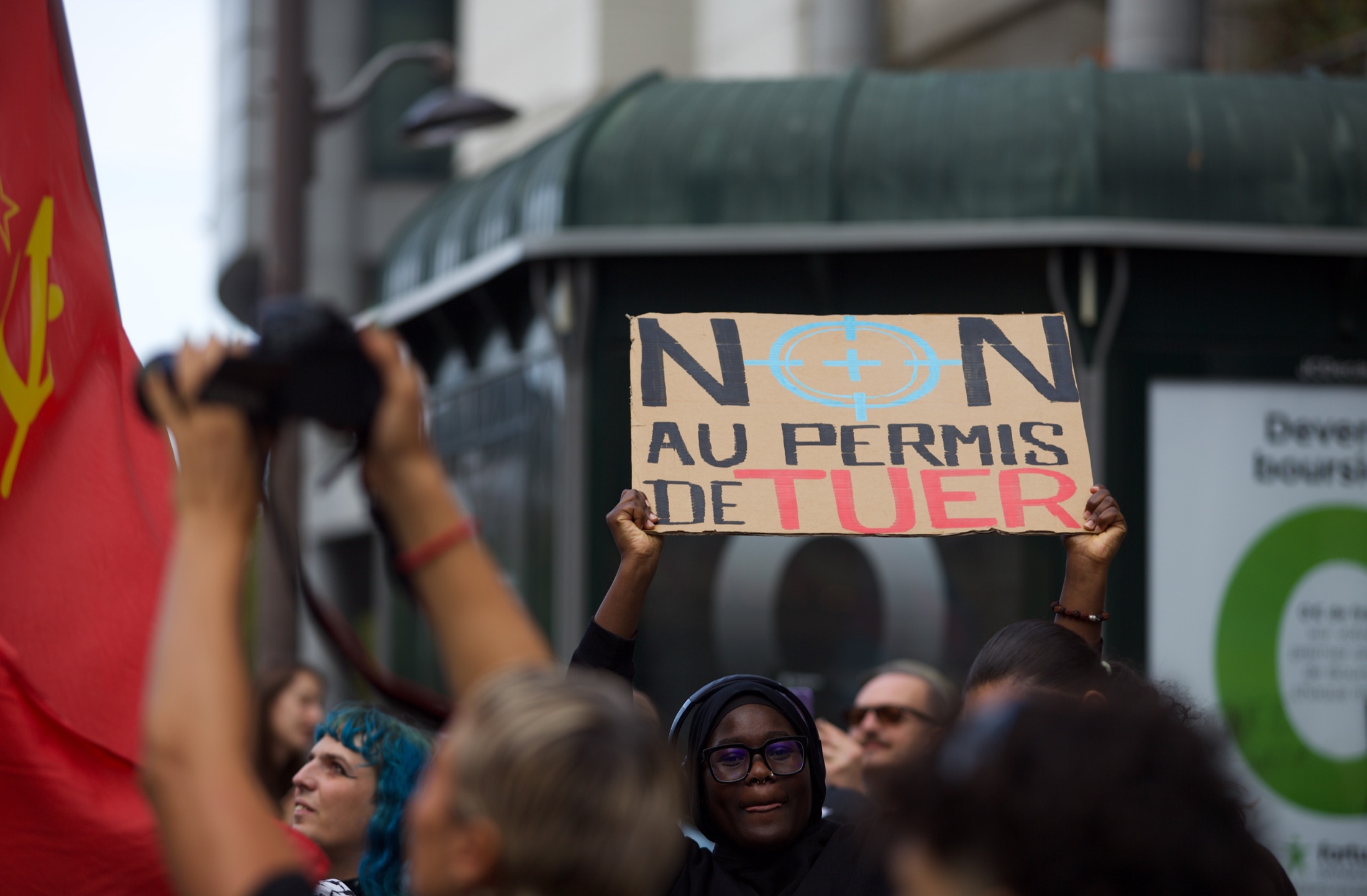Une manifestante brandit une pancarte en carton « Non au permis de tuer », dont le O est remplacé par une cible