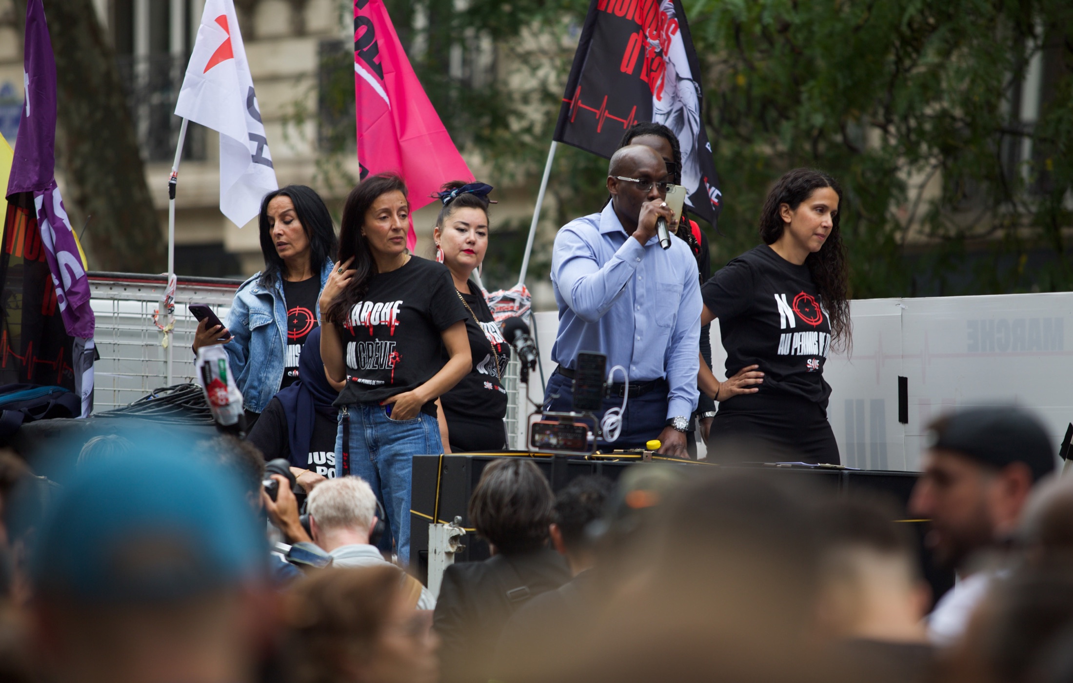 Prises de parole depuis un camion-tribune, devant des drapeaux d’organisations et une banderole « Non au permis de tuer »